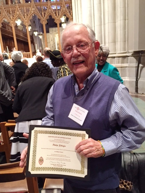 old man wearing a sweater vest and holding a certificate
